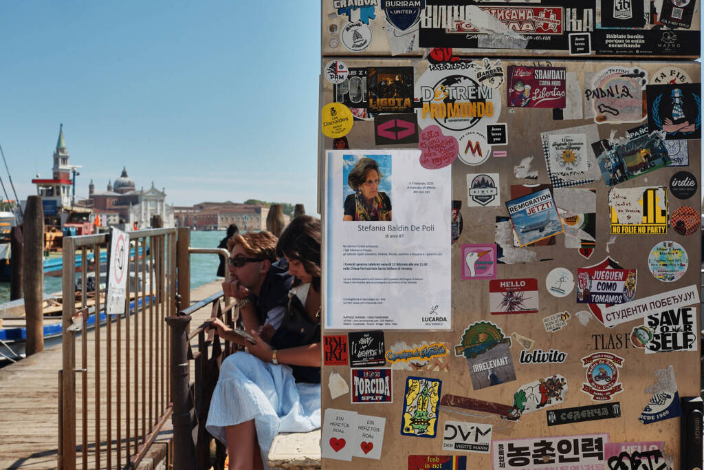 Palo e bacheca ricoperti di adesivi, volantini e avvisi in una calle di Venezia