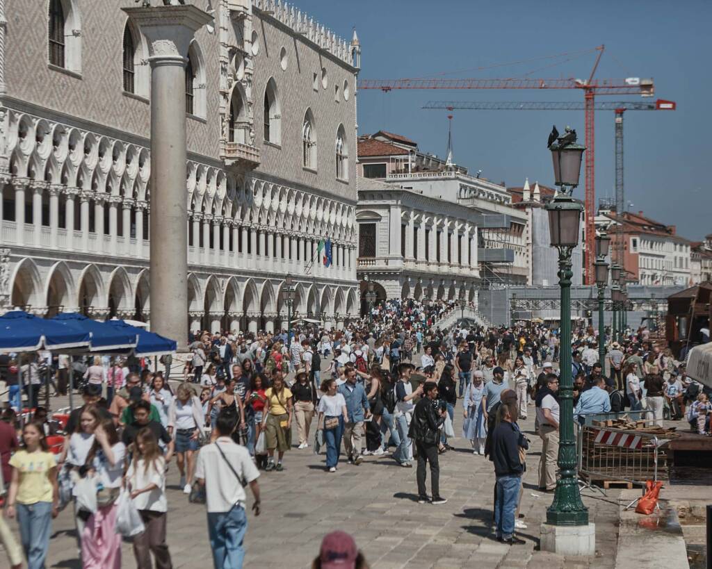 Folla compatta di visitatori cammina sulla Riva degli Schiavoni davanti ai palazzi veneziani