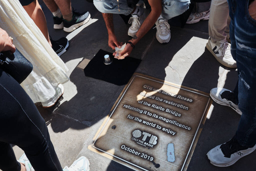 Piedi di passanti attorno a una targa commemorativa incastonata nella pavimentazione veneziana