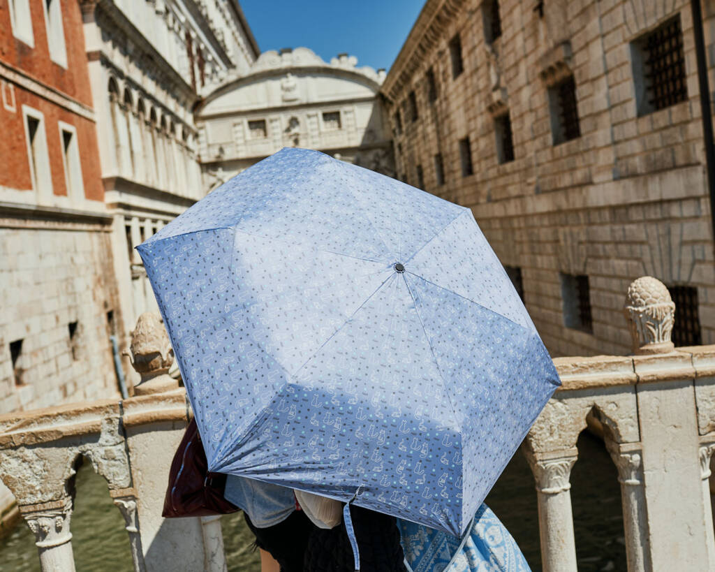 Persona con un ombrello azzurro aperto davanti al Ponte dei Sospiri affollato